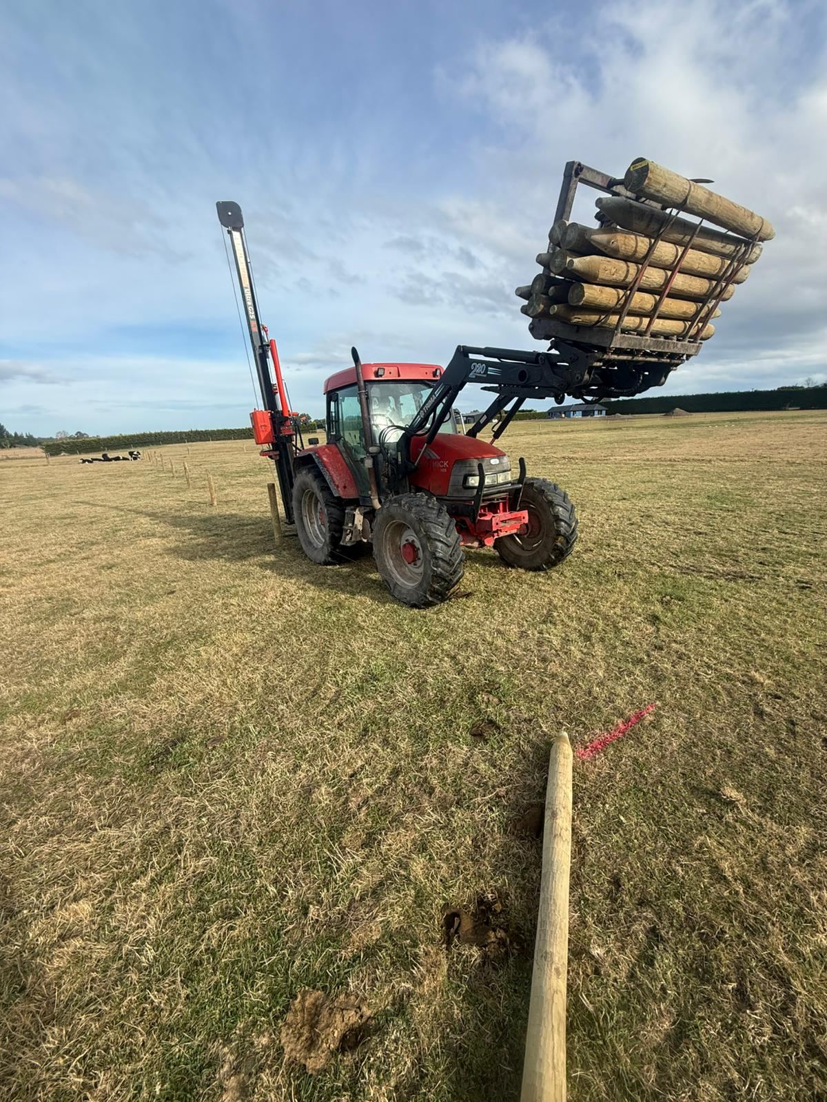 The tractor and post driver parked on a fence line, timber posts stacked ready